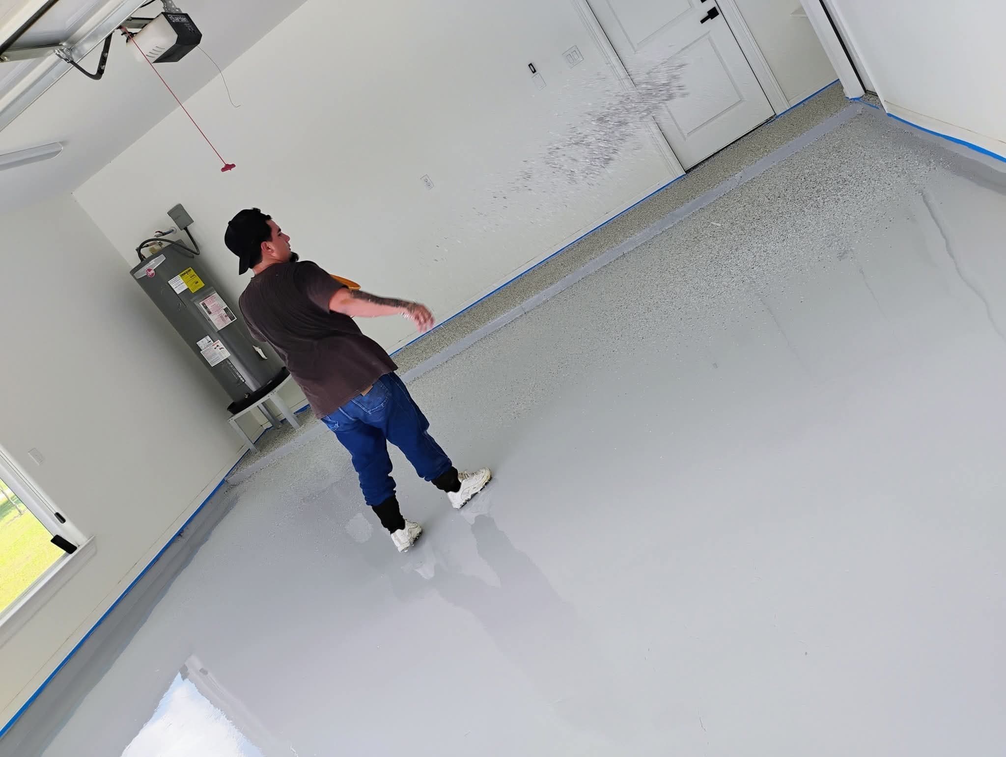 A member of the crew working across a freshly coated garage floor, wall edges still masked off.