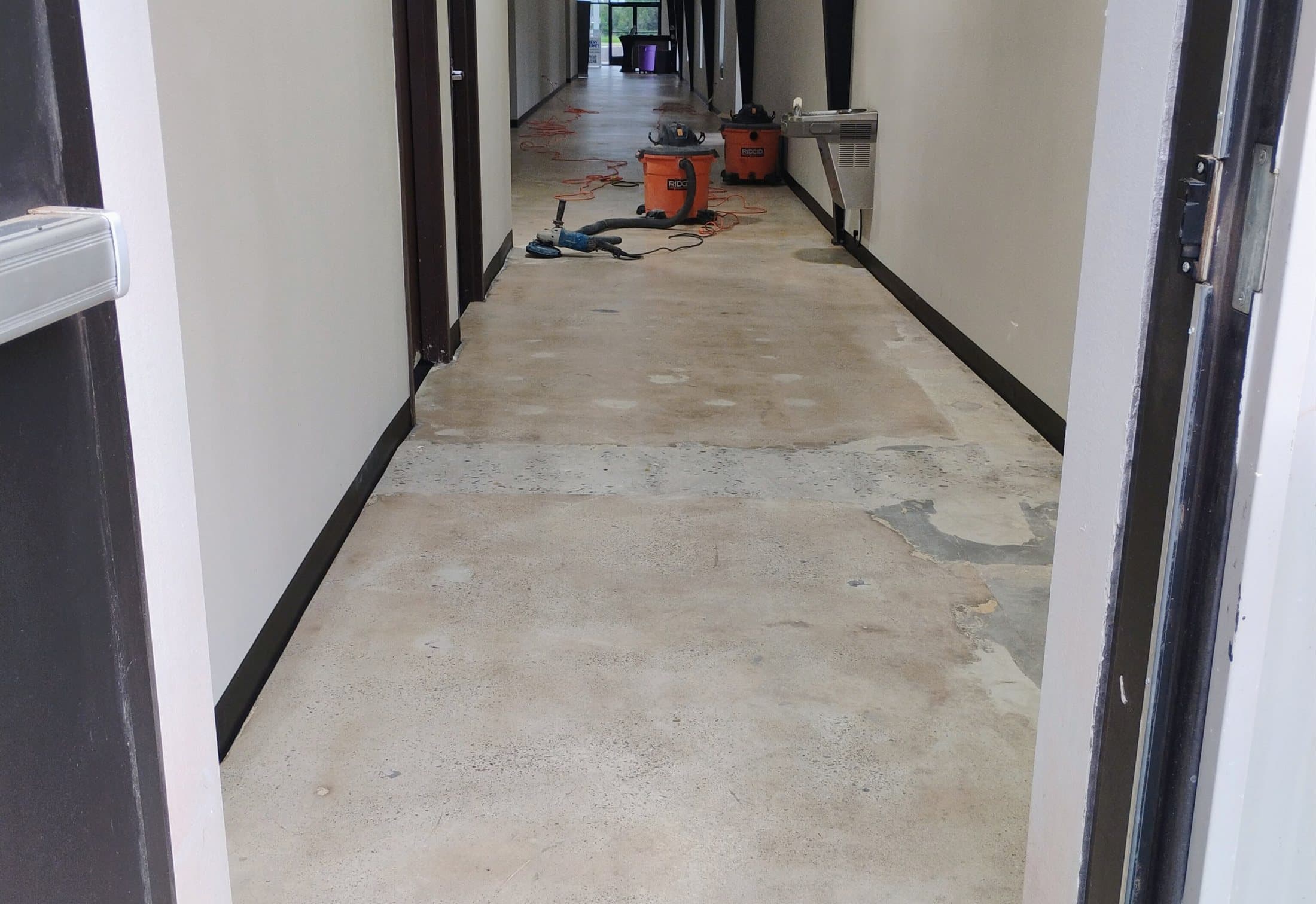 Bare, patched concrete floor along a commercial corridor before coating.