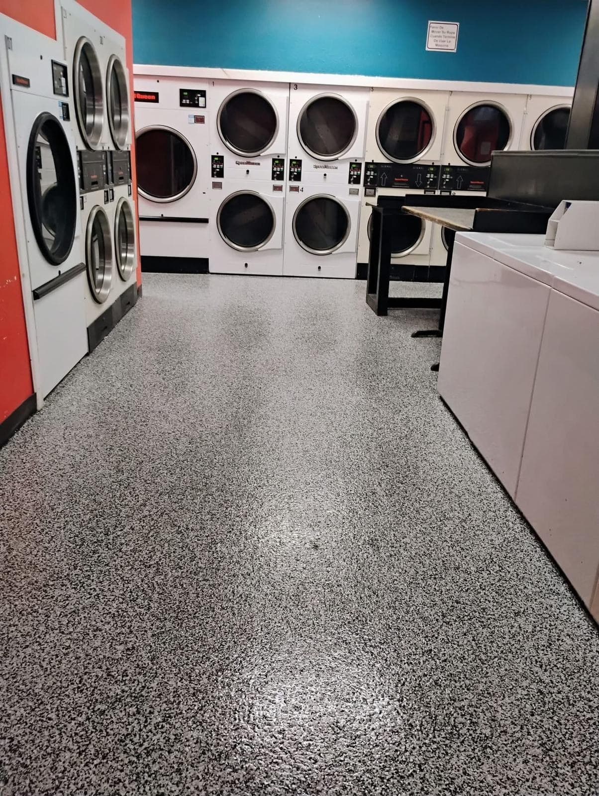 Grey and black flake floor running between the washers and dryers of a laundry facility.