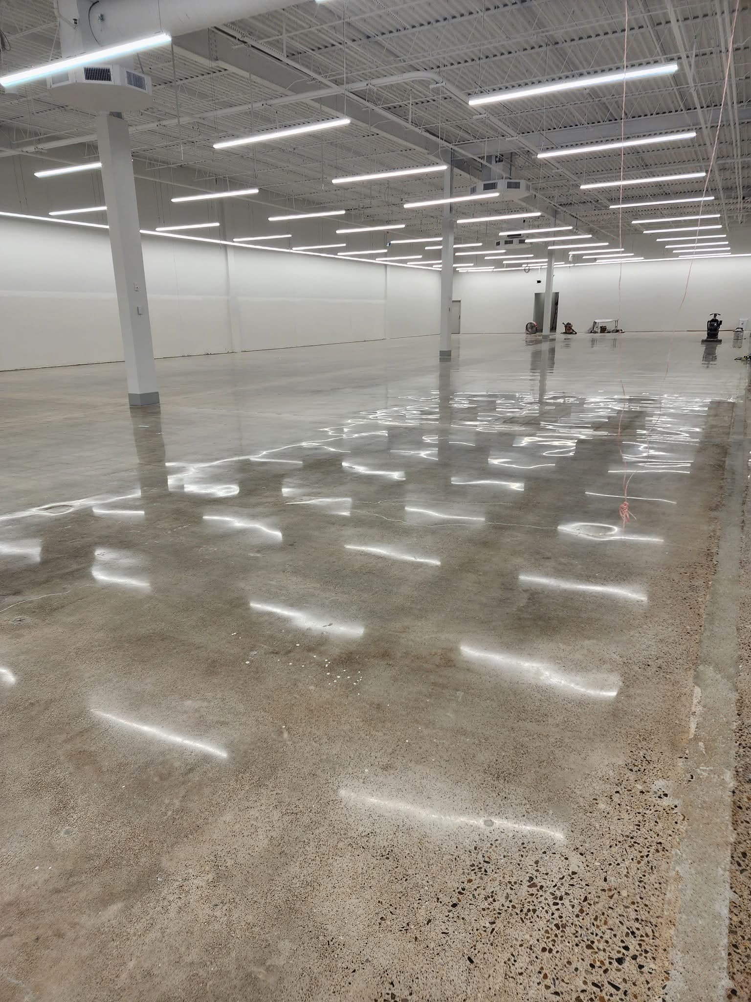 Polished concrete floor across a large open commercial interior, ceiling lights reflected down its length.