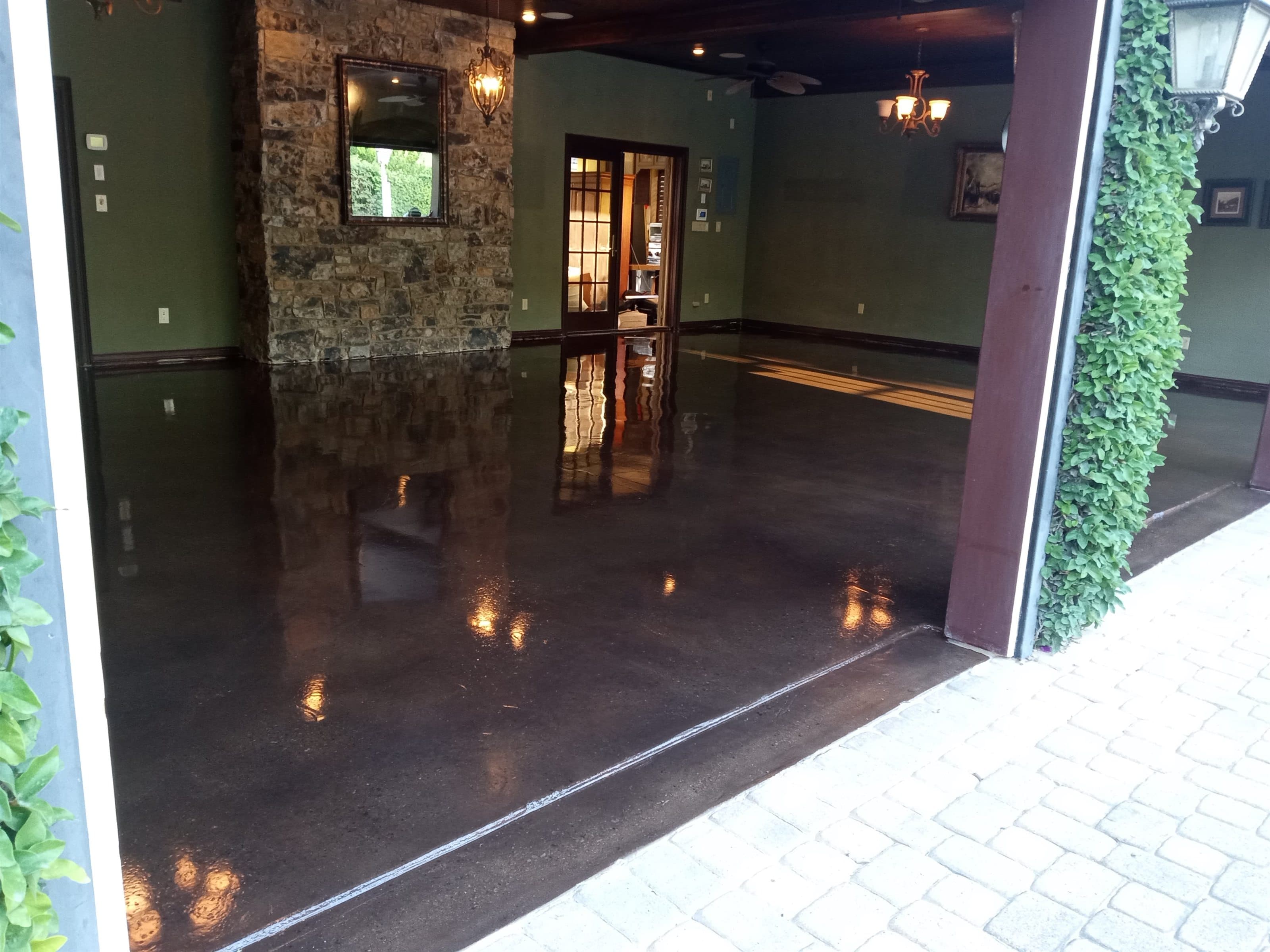 Dark, high-gloss decorative concrete floor under a covered patio, opening onto a paver walkway.