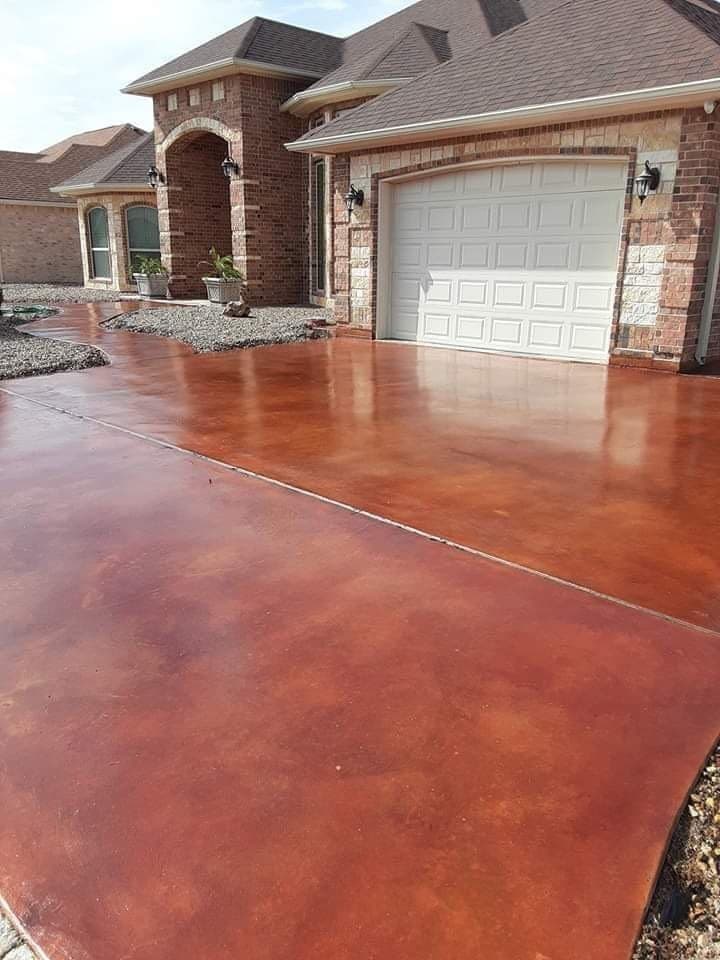 Red-brown stained concrete driveway running up to the garage of a brick home.