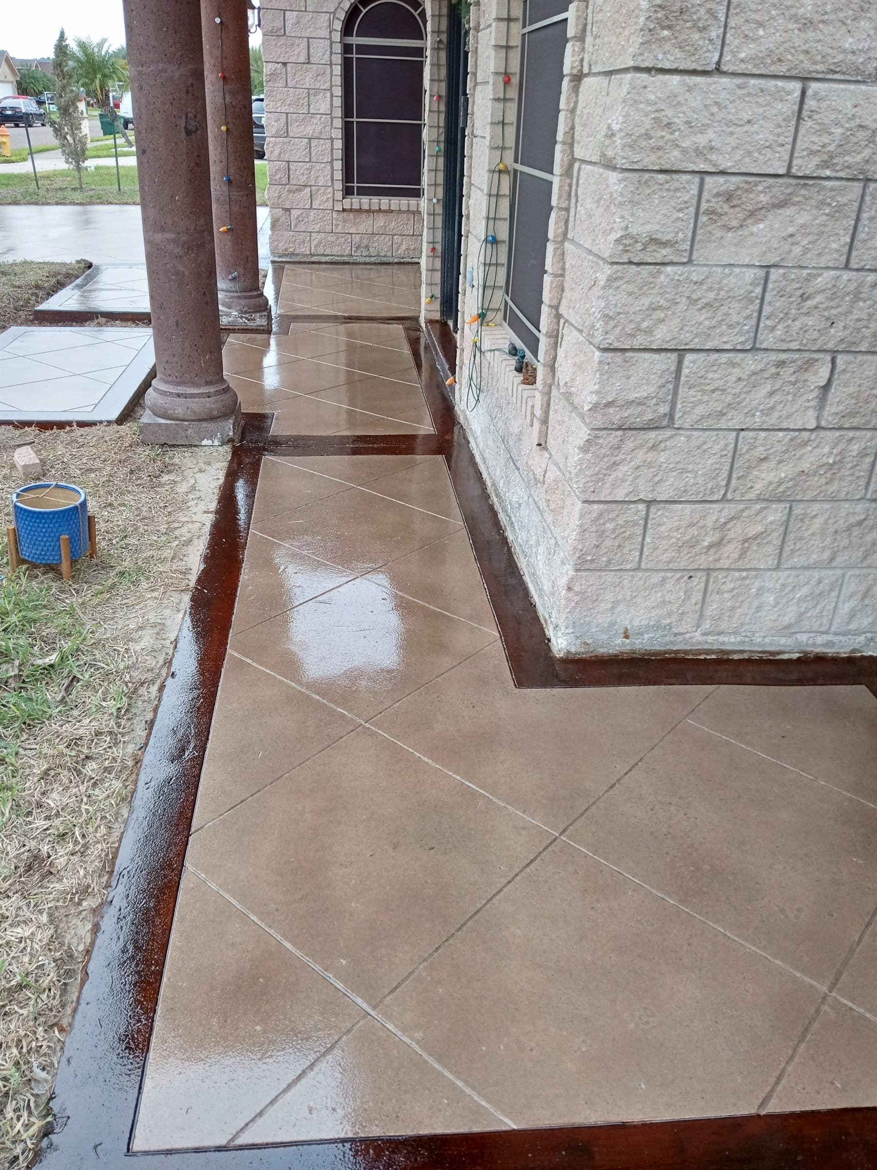 Tan scored and stained concrete walkway with a dark border, wrapping the front of a home.