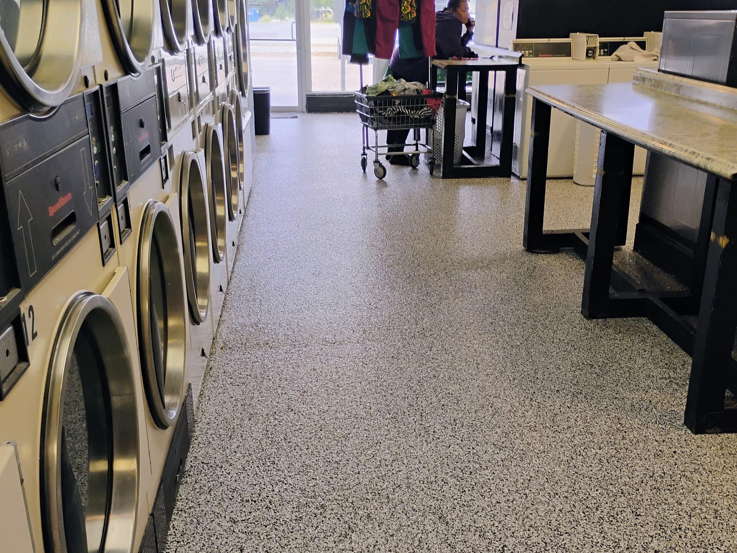 Black and white flake floor running between the machines and folding benches of a laundry facility.