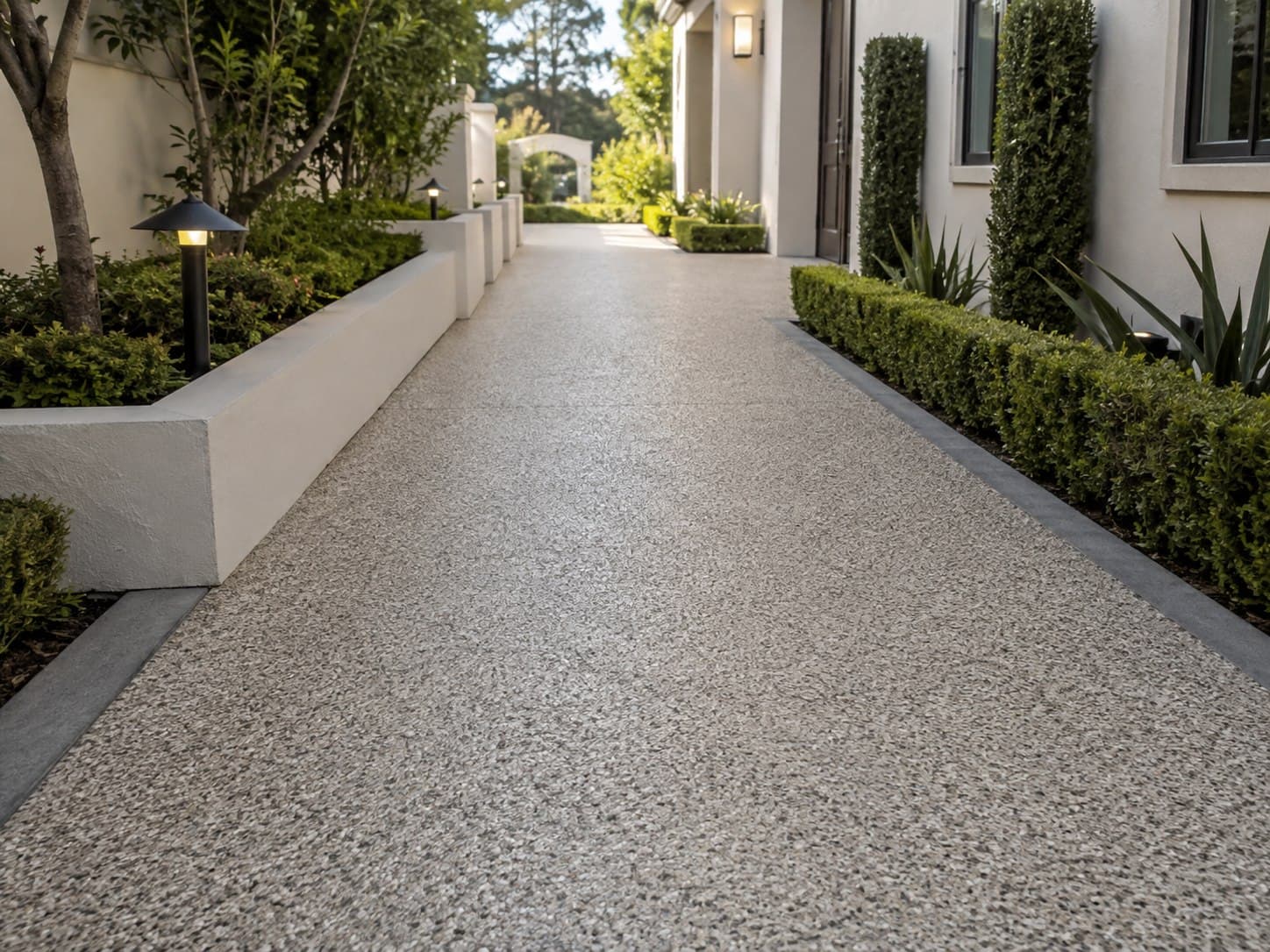 Pale quartz-broadcast walkway running between clipped hedging alongside a house.
